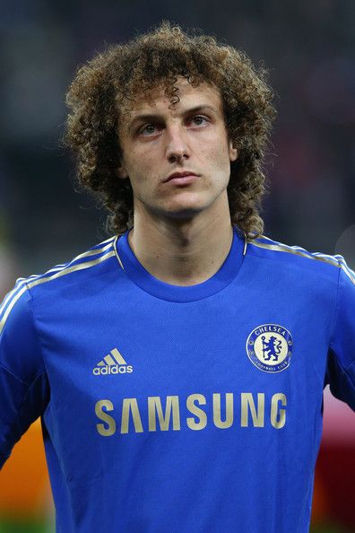 a man with curly hair wearing a blue soccer jersey and looking off to the side