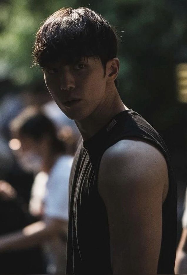 a young man standing in front of a crowd wearing a black shirt and looking at the camera