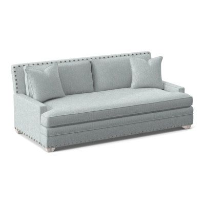 a light blue couch with pillows on the arm and back cushions, in front of a white background