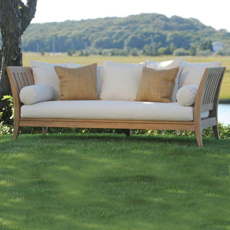 a couch sitting on top of a lush green field next to a tree with lots of pillows