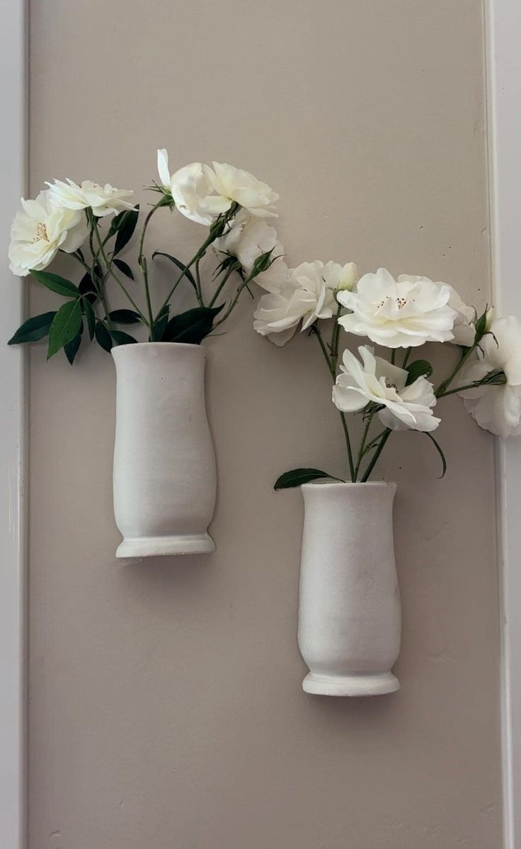 three white vases with flowers in them hanging on the wall next to each other