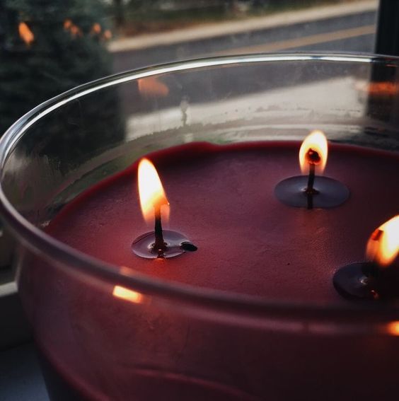 three lit candles in a glass bowl on a window sill