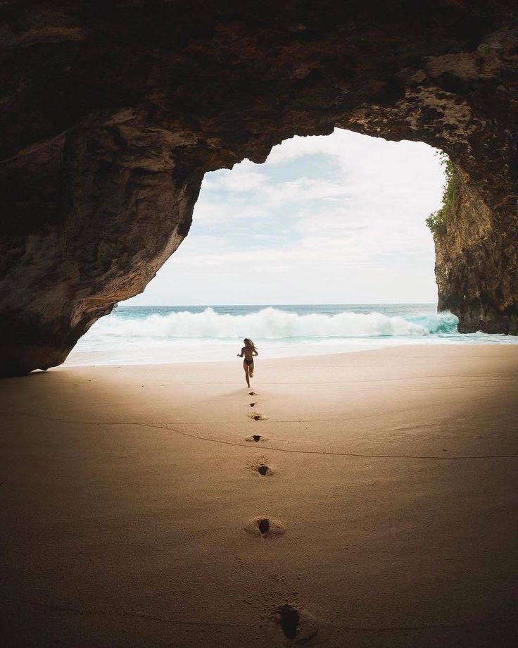 a person is walking on the beach towards an arch in the sand with footprints leading into the water