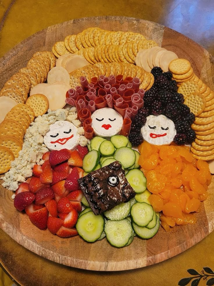 a wooden plate topped with fruit and veggies next to crackers on top of a table