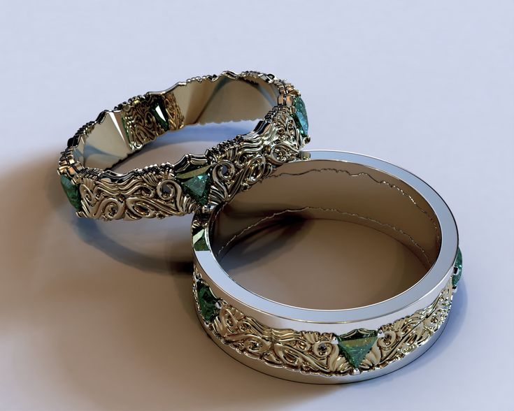 two wedding rings sitting next to each other on top of a white surface with gold and green accents