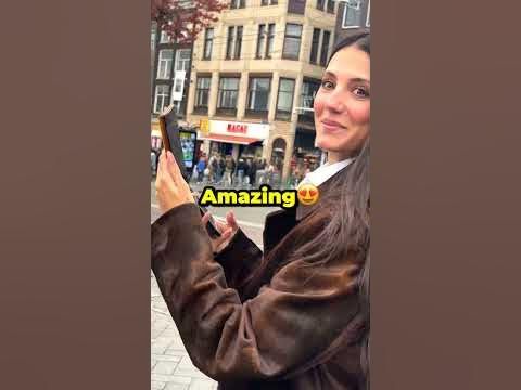 a woman standing in front of a building holding up a cell phone with the words amazing on it