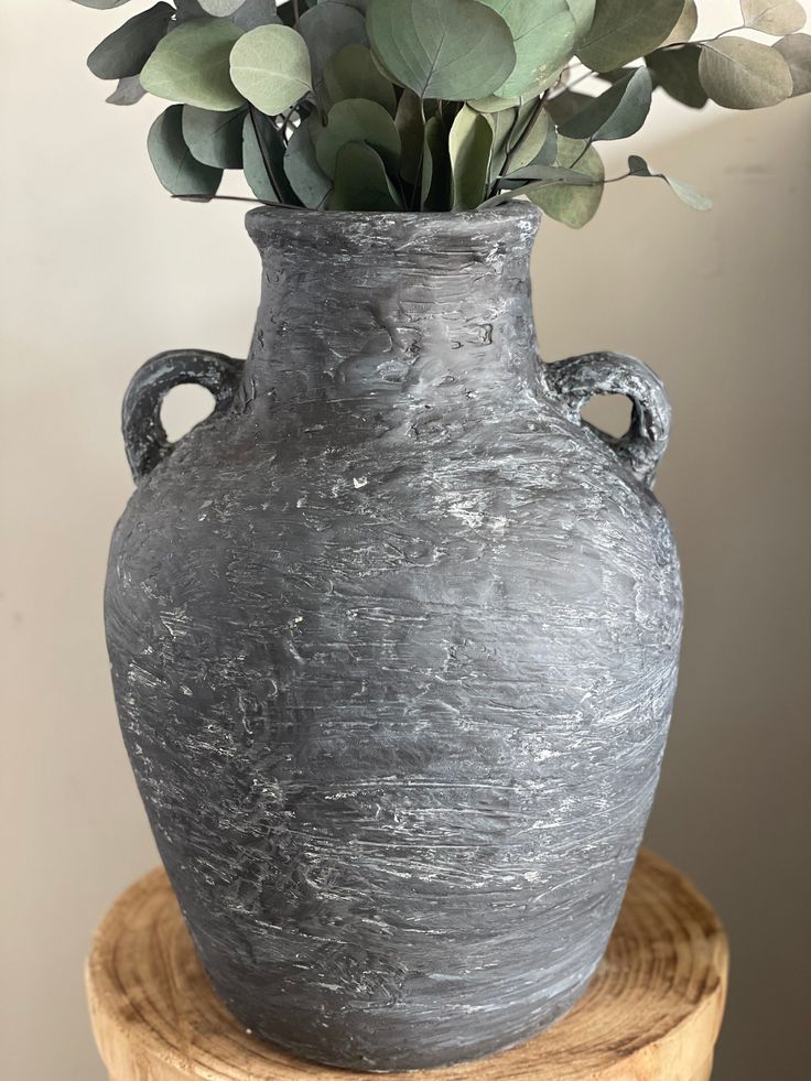 a gray vase with some green plants in it