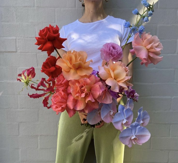 a woman holding a bouquet of flowers in front of her face and wearing green pants