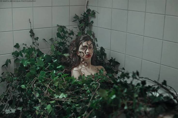 a woman with painted face and body surrounded by greenery in a tiled bathroom area