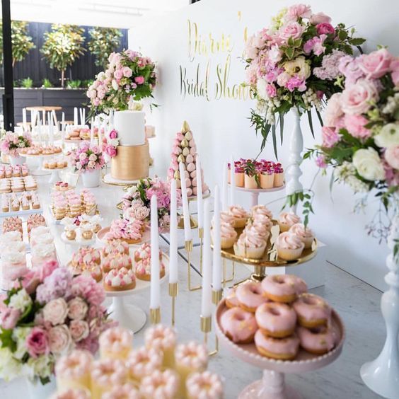 a table topped with lots of donuts covered in frosting next to tall vases filled with flowers