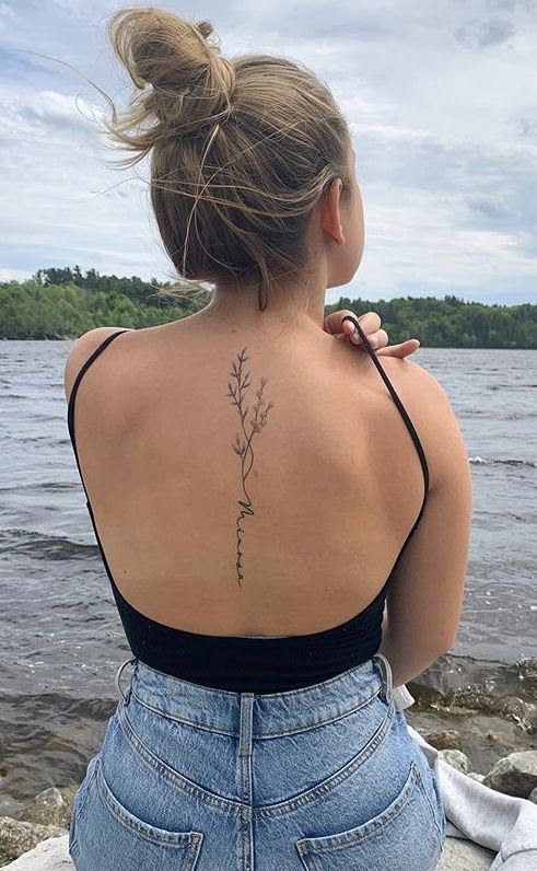 the back of a woman's neck with a flower tattoo on her left shoulder