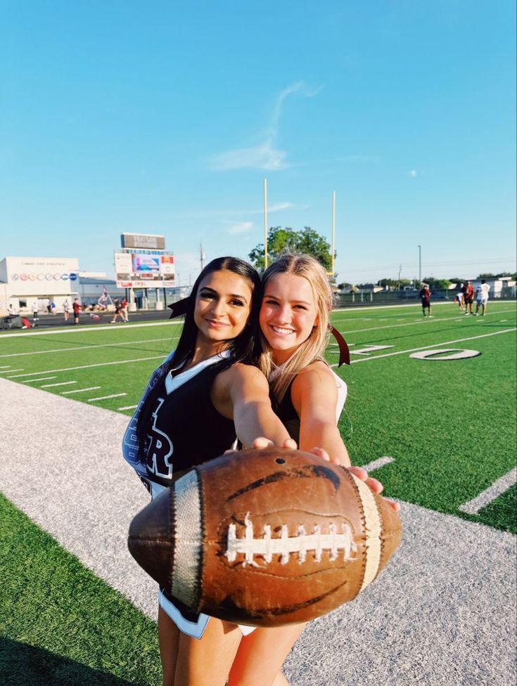 two girls are posing with a football on the field