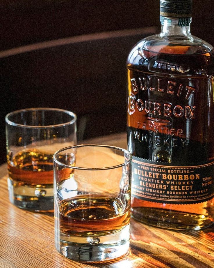 a bottle of bourbon sitting on top of a wooden table next to two glasses filled with liquid