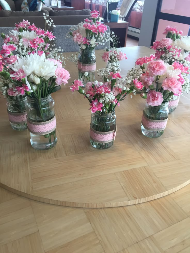 pink and white flowers are in mason jars on a round table with wood flooring