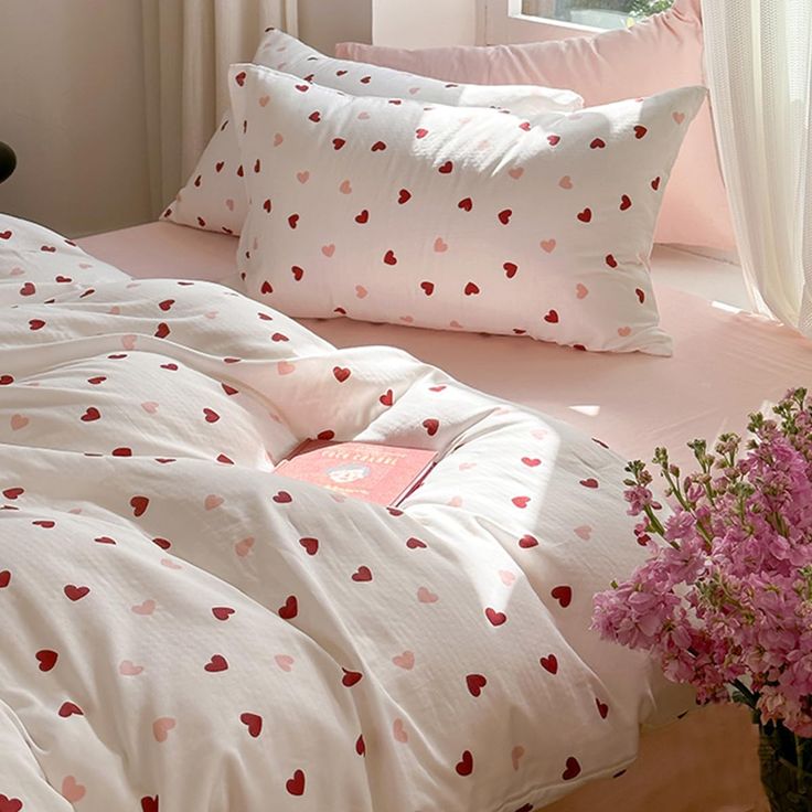 a bed with hearts on it and pink flowers in a vase next to the bed