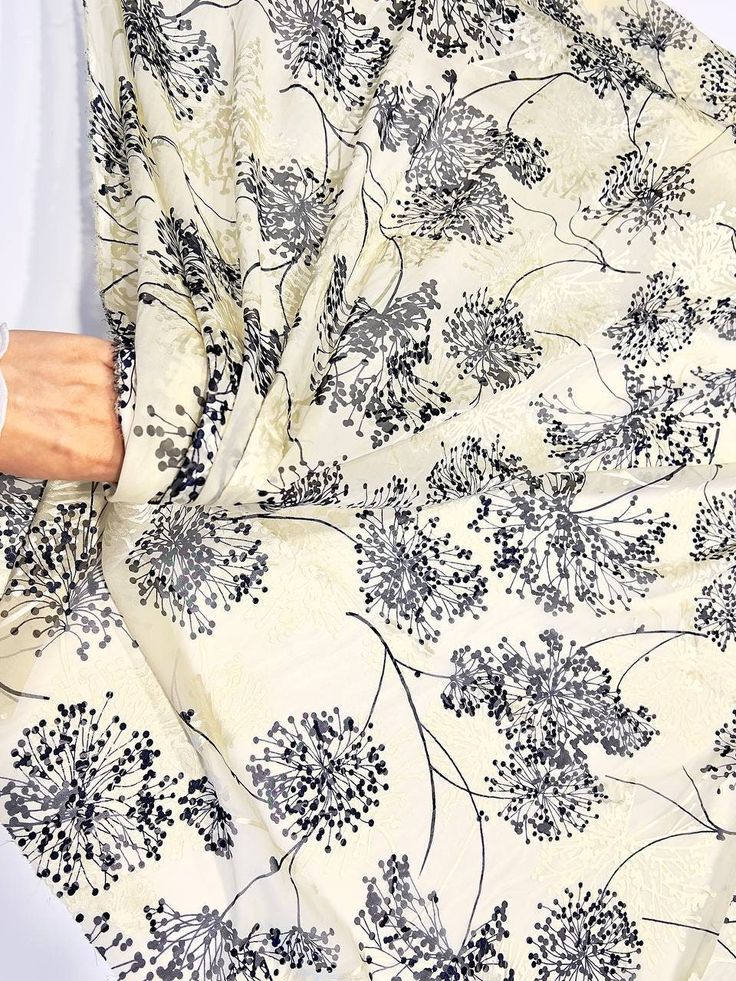 a woman's hand is holding onto a white and black floral print fabric with flowers on it