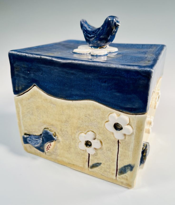 a ceramic box with flowers and a bird on top