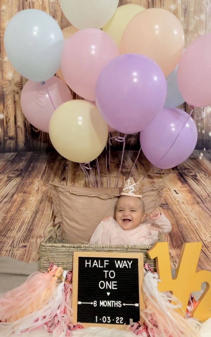 a baby in a basket with balloons and a sign that says half way to one month