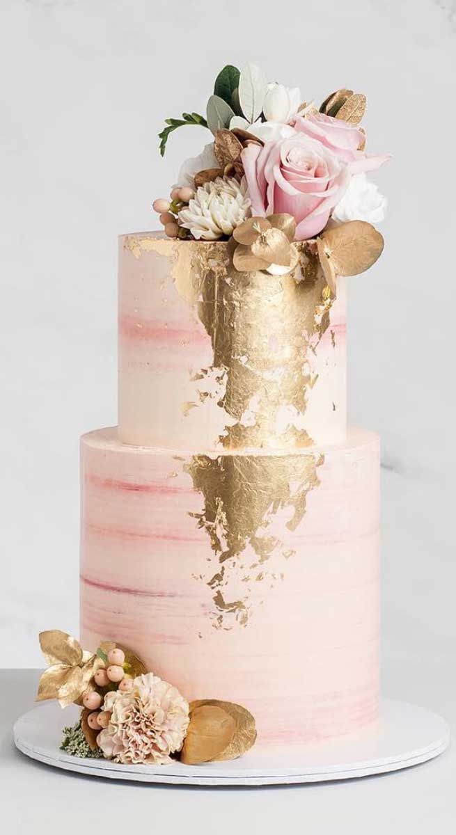 a pink and gold wedding cake with flowers on top