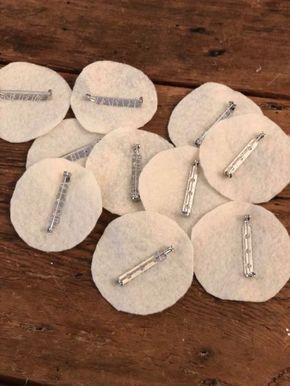 several pieces of white felt with silver pins on them sitting on top of a wooden table