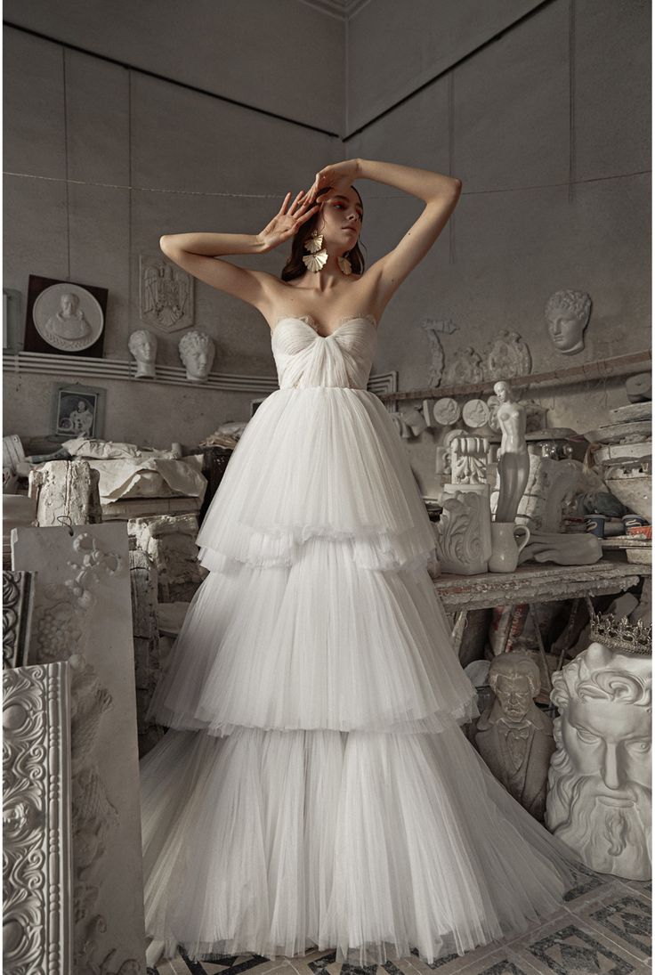 a woman in a white wedding dress standing next to a pile of vases and other items