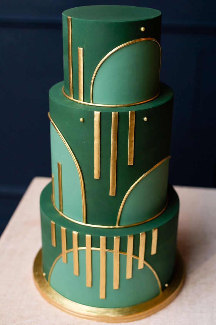 a three tiered green and gold cake on top of a white cloth covered table