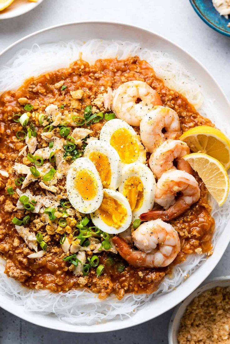 a white plate topped with rice covered in shrimp and boiled eggs next to lemon wedges