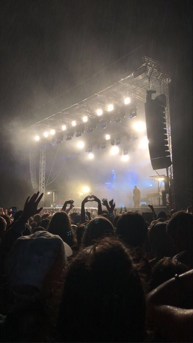 a large crowd at a concert with their hands up in the air and lights on