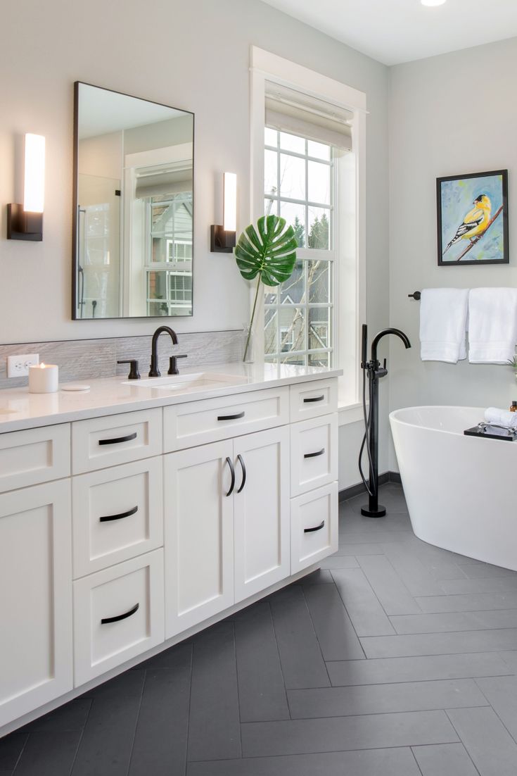 a large white bath tub sitting next to two sinks in a bathroom under a window