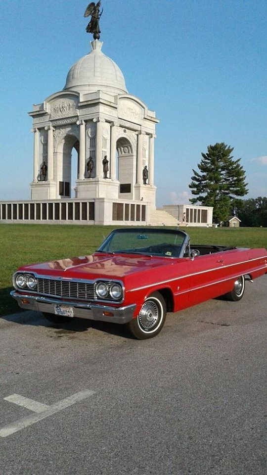 an old red car parked in front of a monument