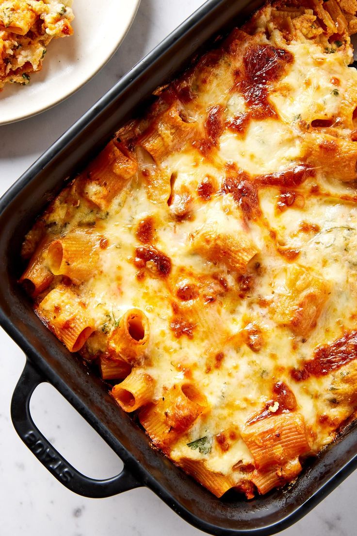 a casserole dish with meat and cheese on the side next to a plate