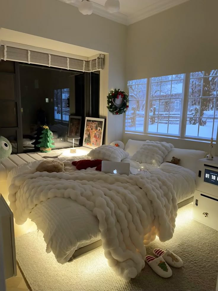 a bed that is made up with blankets and lights on the headboard, in front of two windows