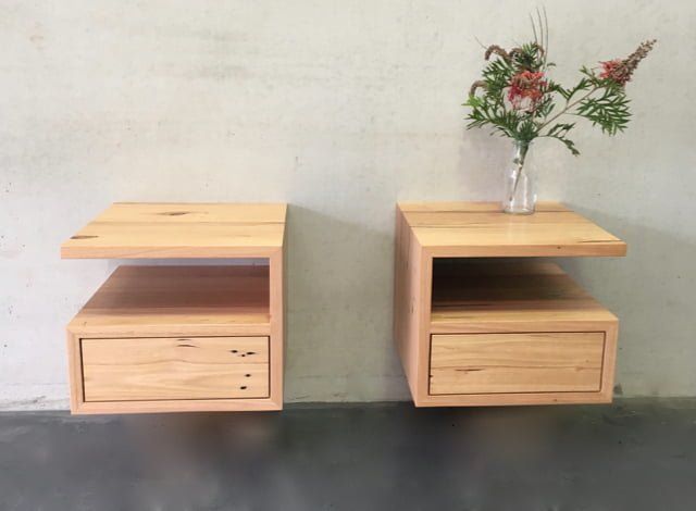 two wooden nightstands with flowers in them on a table next to a white wall