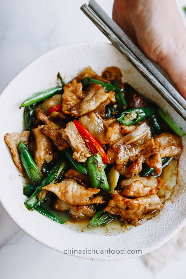 someone holding chopsticks over a bowl of food with meat and veggies