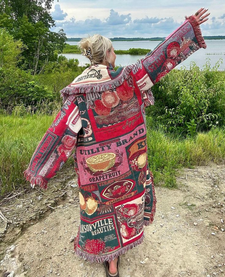 a woman in a red and black dress standing on a dirt road with her arms outstretched