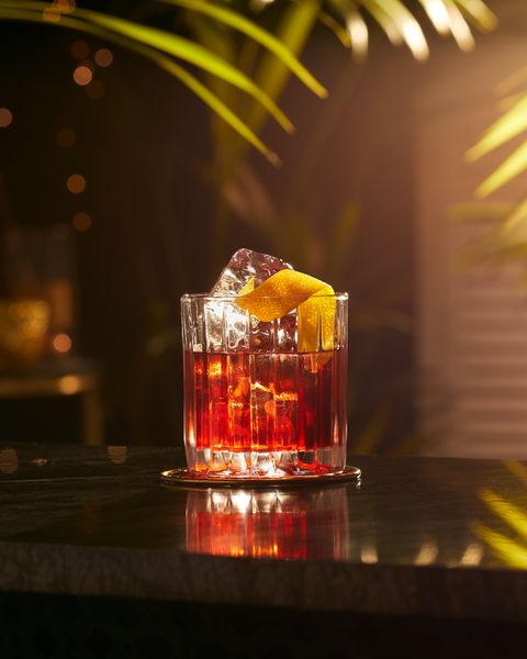 a glass filled with red liquid and an orange slice on top of the drink is sitting on a table