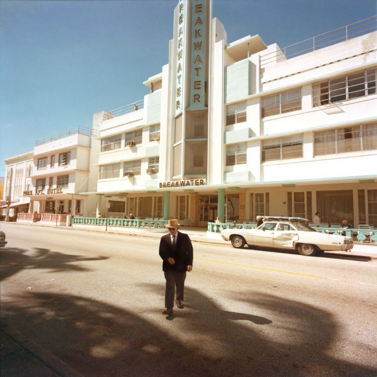 a man is walking down the street in front of a large building with many balconies