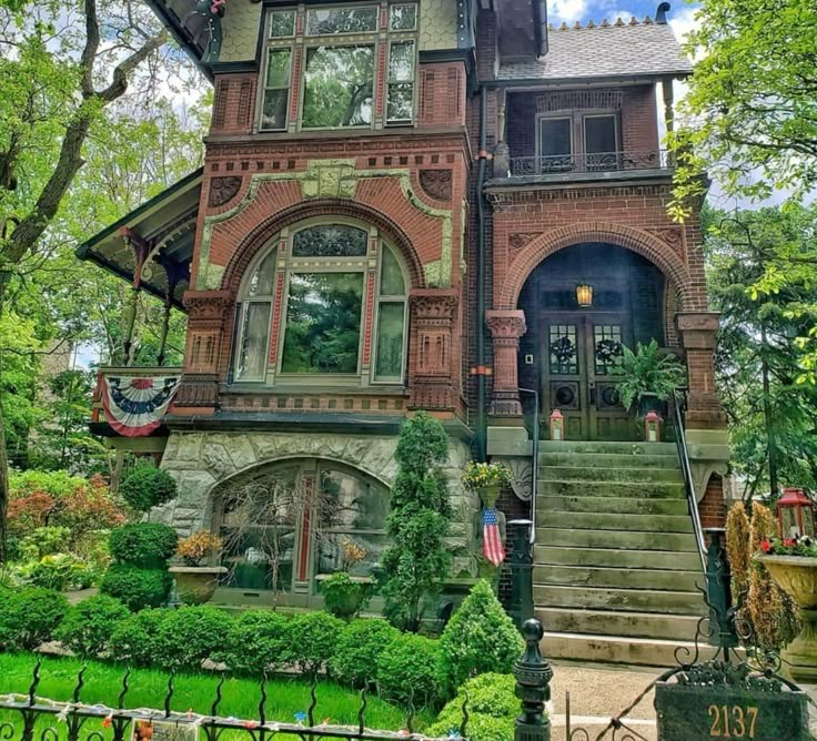 an old victorian house with lots of windows and plants on the front steps, surrounded by lush green trees