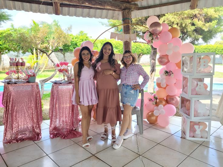 three women standing next to each other in front of a table with balloons on it