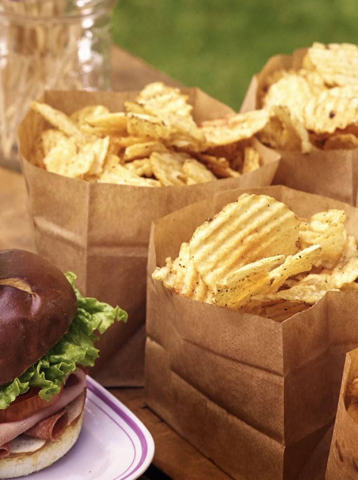 a table topped with brown paper bags filled with chips and a sandwich covered in lettuce