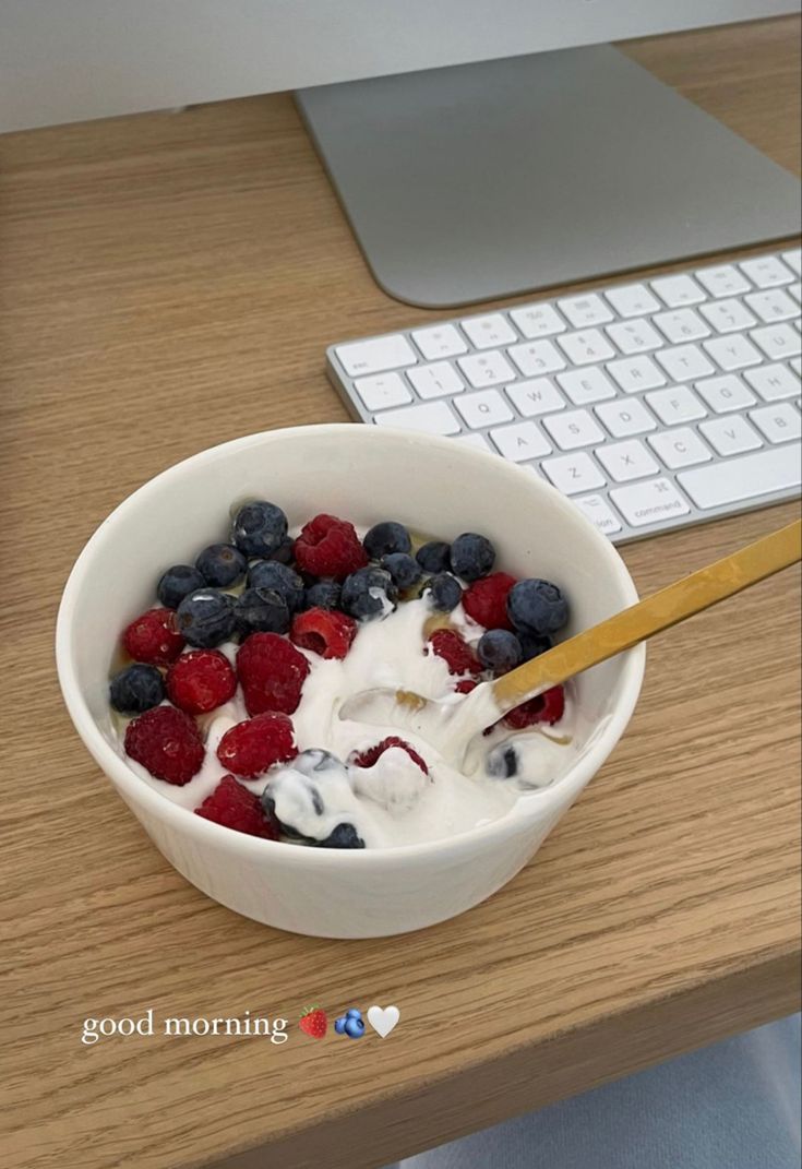 a bowl of fruit with yogurt and berries in front of a computer keyboard