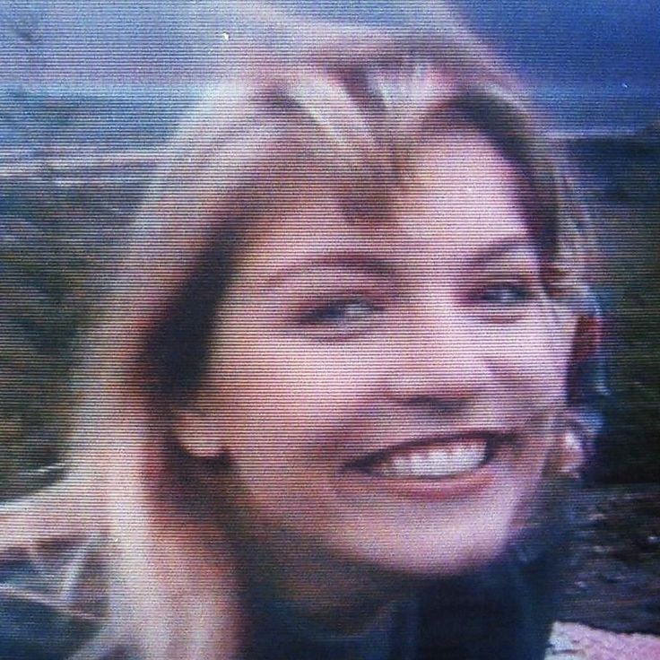 a blurry photo of a woman smiling with mountains in the back ground behind her