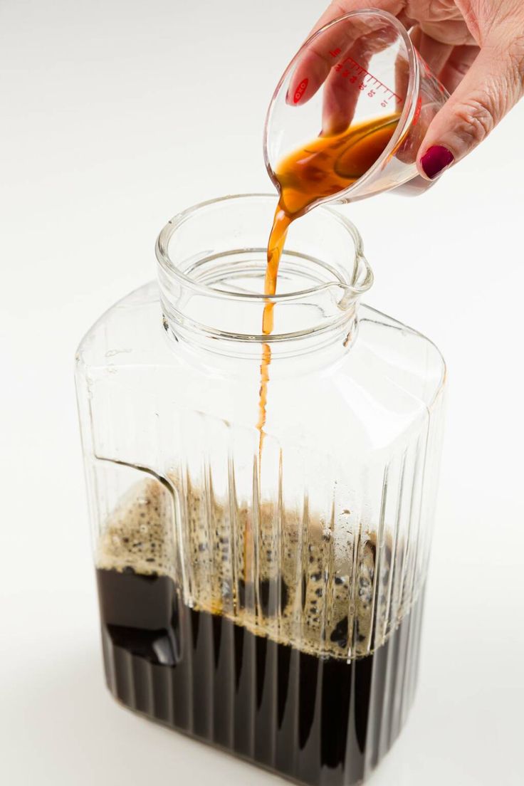 a person pours coffee into a glass jar filled with ice and liquid on a white surface