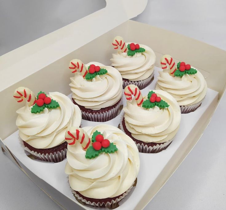 six cupcakes with white frosting and candy decorations on them in a box