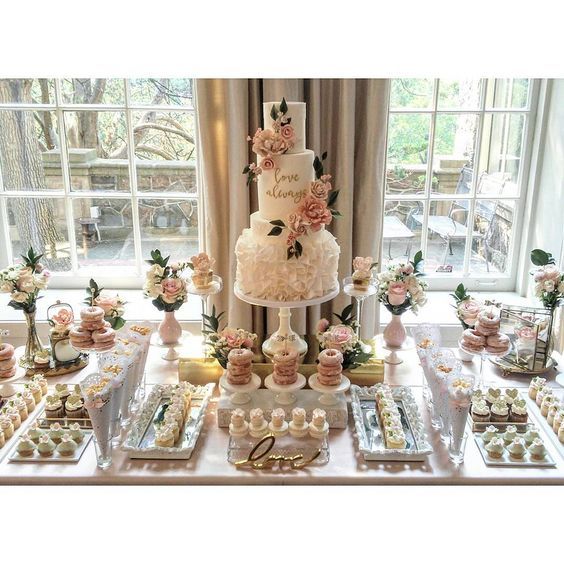 a table topped with lots of cakes and cupcakes next to a window filled with windows