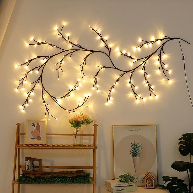 there is a wall decoration with lights on the branches and plants in front of it