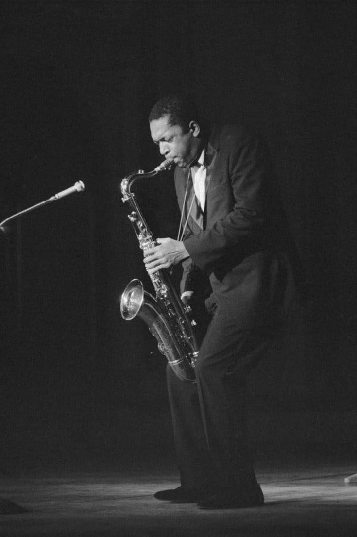 a man in a tuxedo playing a saxophone on stage with a microphone behind him