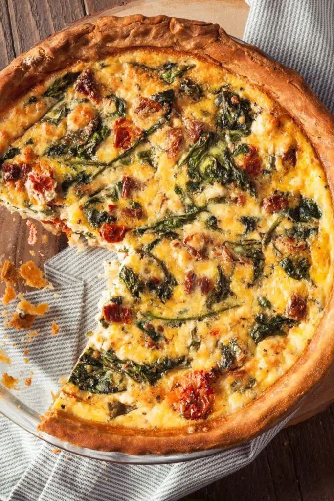 a quiche with spinach and cheese is cut in half on a wooden table