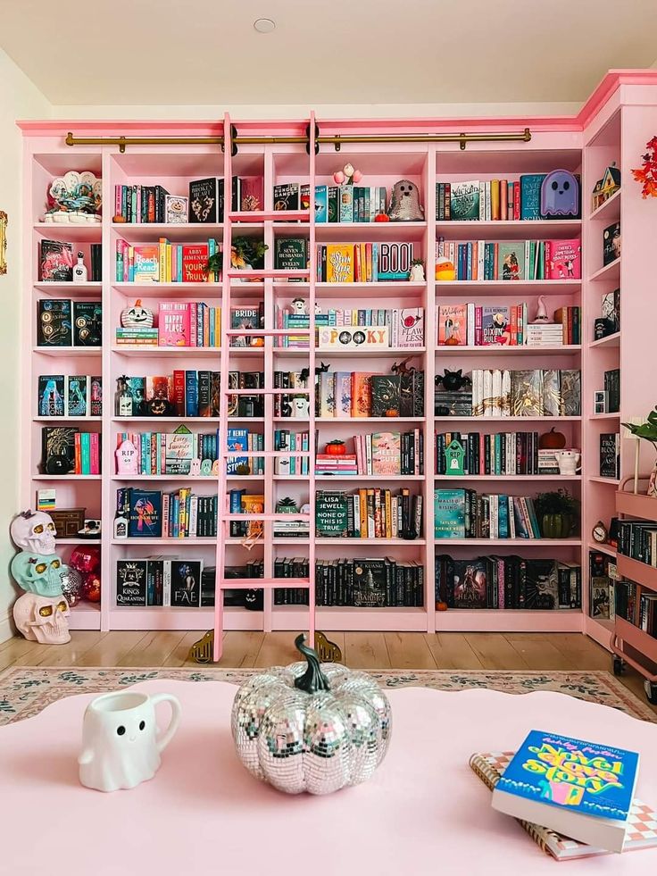 a pink bookcase filled with lots of books next to a white elephant statue on top of a table