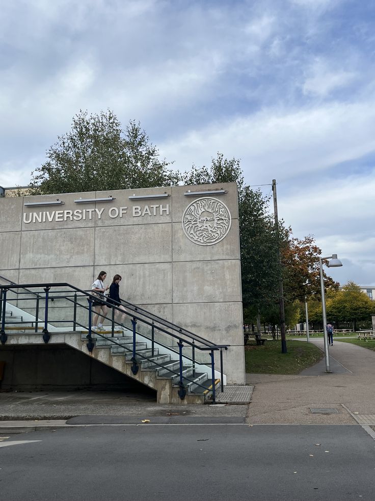 two people are sitting on the stairs in front of an university of bath sign and building